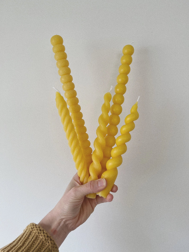 Hand holding three twisted yellow candles against a plain background