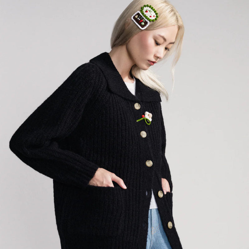 Person wearing a black cardigan with decorative buttons on a plain background