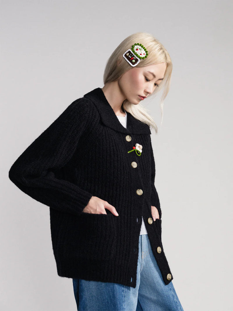 Person wearing hanself from basel hair clips and a black cardigan with decorative buttons on a plain background