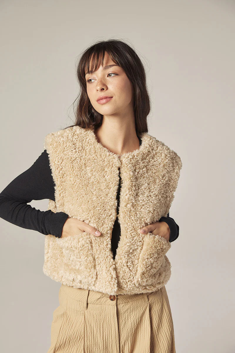 Woman wearing a beige wool vest against a plain background