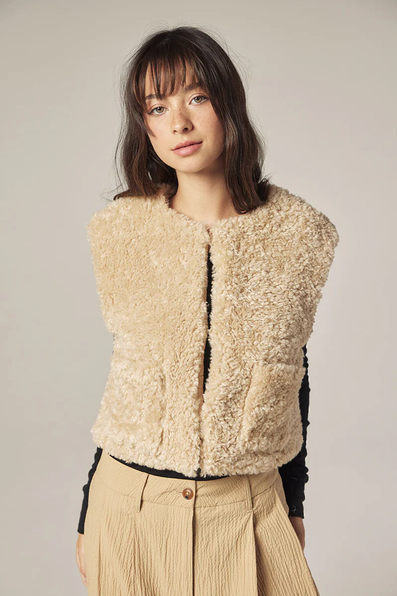Woman wearing a beige wool vest against a plain background