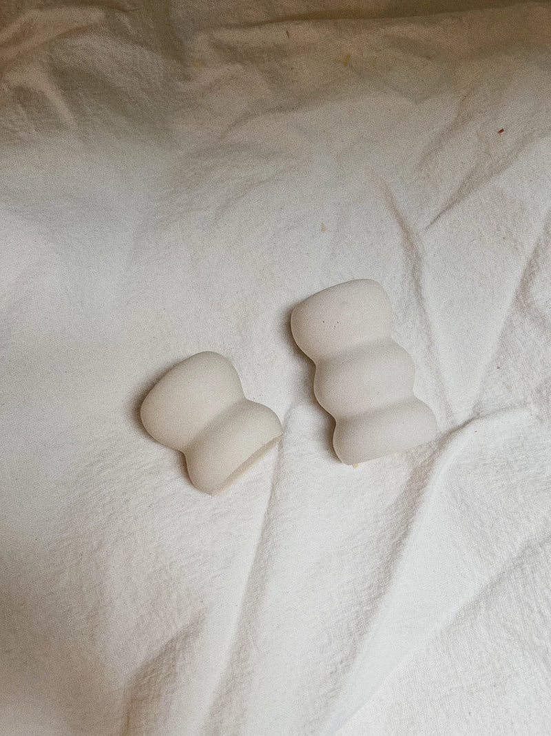 two white wavy candels holders against white fabric