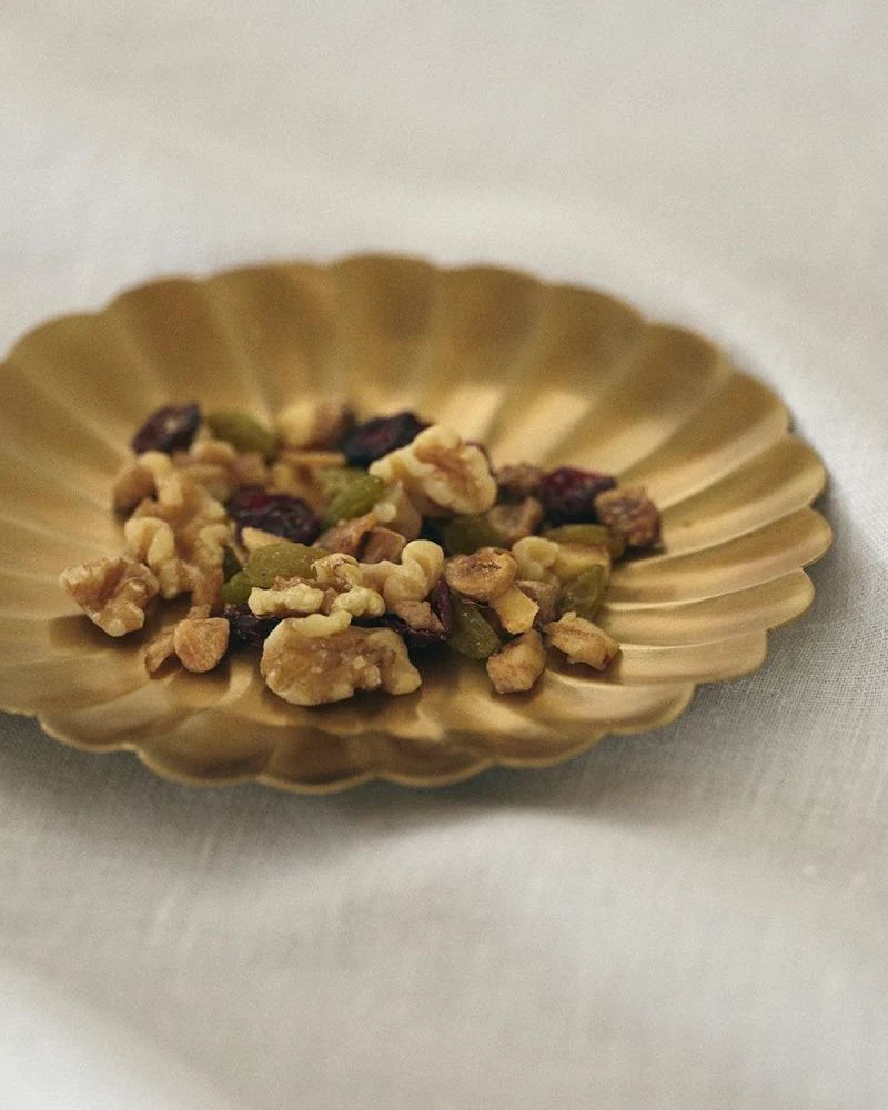 Nuts and dried fruits on a brass plate with a white background.

Fog Linen round petal brass plate tray dish serving catch all home decor kitchen Boston gift shop store boutique
