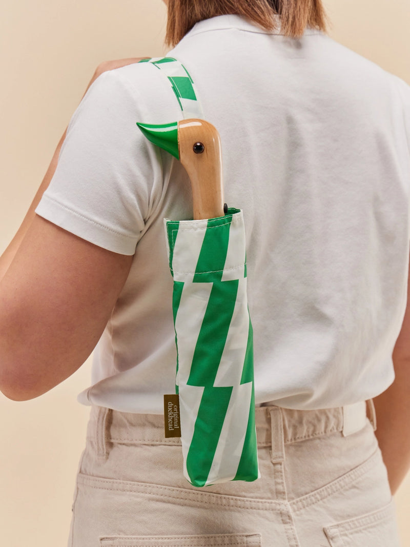 Person holding a green and white striped umbrella against a beige background