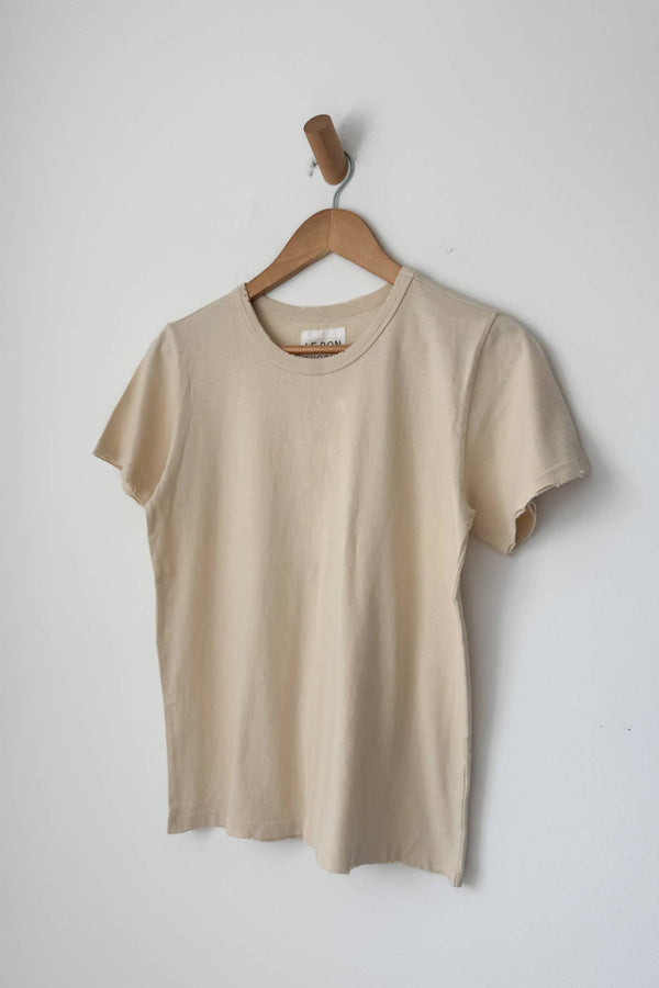 Beige t-shirt on a wooden hanger against a white wall