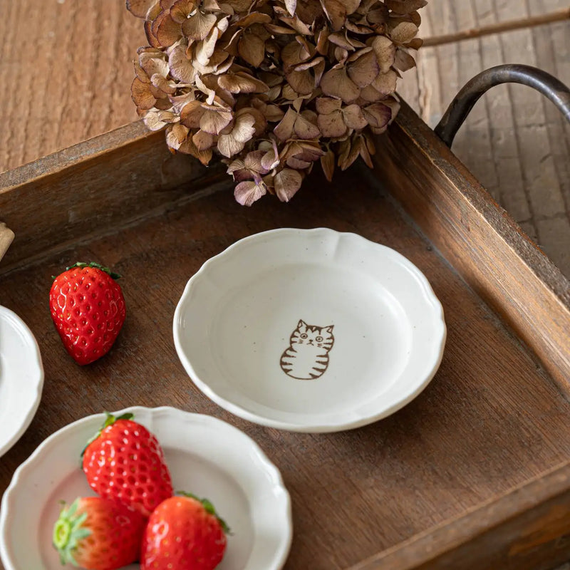 Small ceramic dish with a cat illustration on a wooden surface with strawberries.