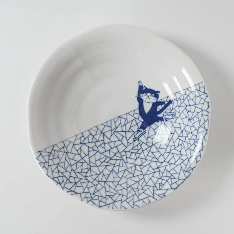 White plate with blue geometric pattern and cat ice skating illustration on a white background