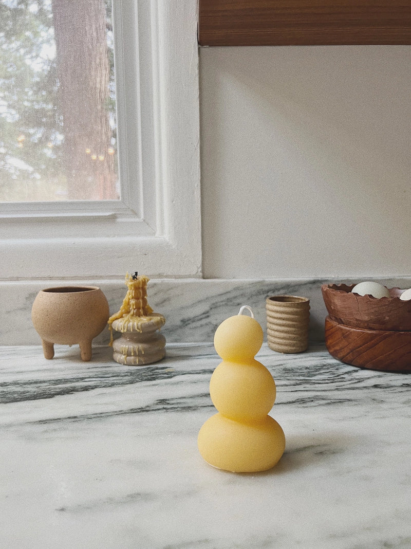 Yellow candle on a marble surface with decorative items in the background