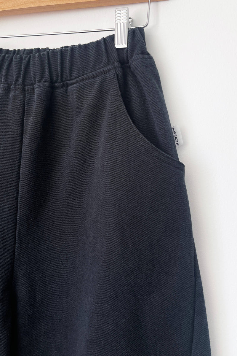 Black pants hanging on a white wall with a wooden shelf above.