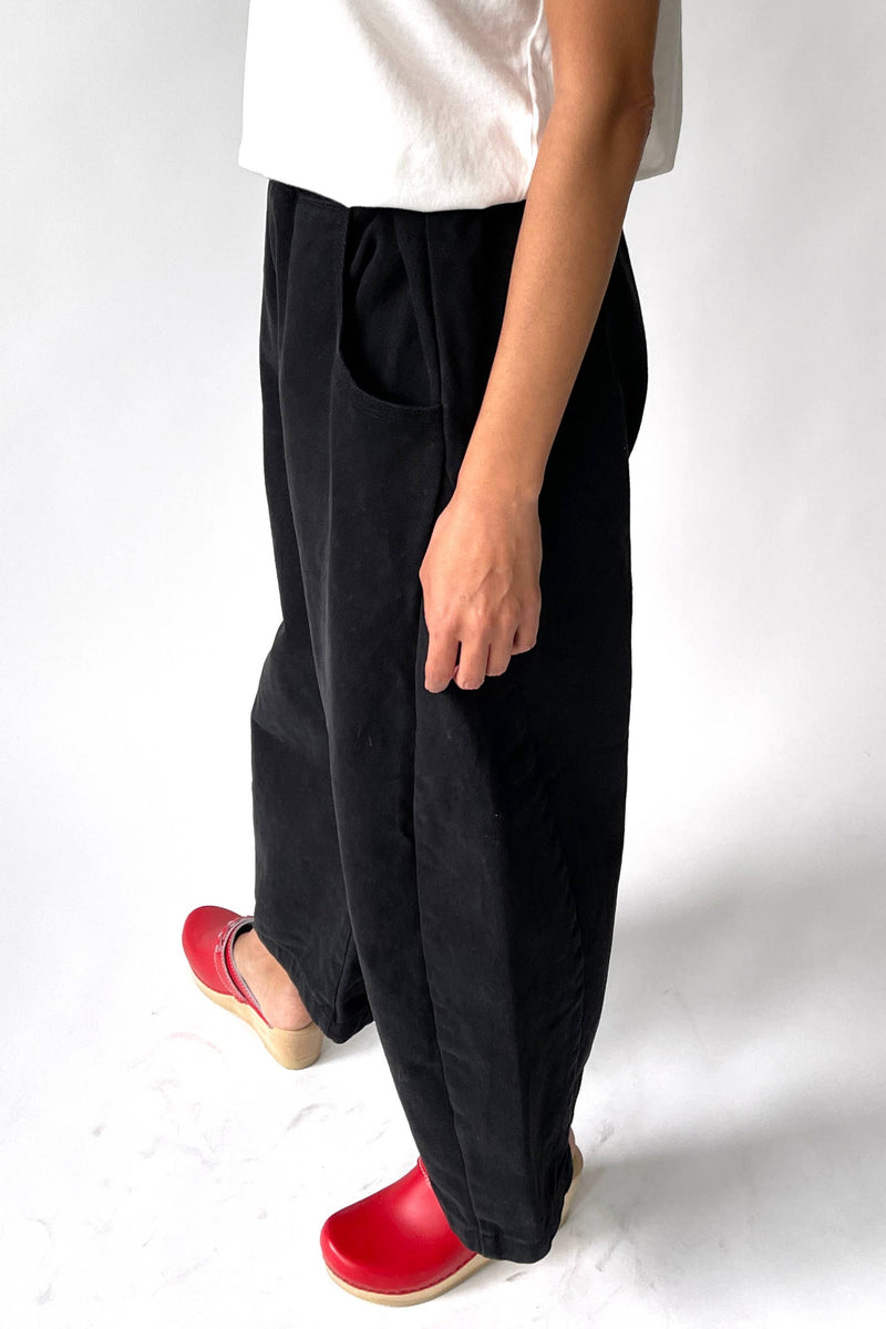 Person wearing black wide-leg pants with a white top and red shoes on a white background