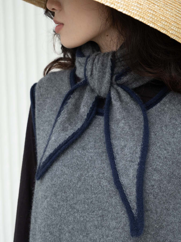 Person wearing a wide-brimmed straw hat and gray sweater vest and short gray and navy scarf