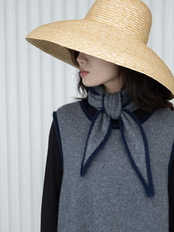 Person wearing a wide-brimmed straw hat and gray sweater vest and short gray and navy scarf