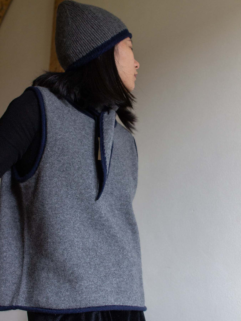 Person wearing a gray sleeveless sweater vest and knit hat against a plain background