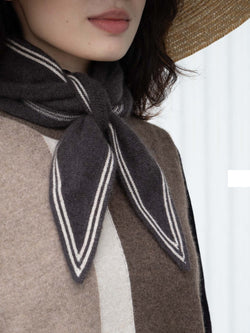 Person wearing a dark brown scarf with white stripes over a brown and beige outfit.