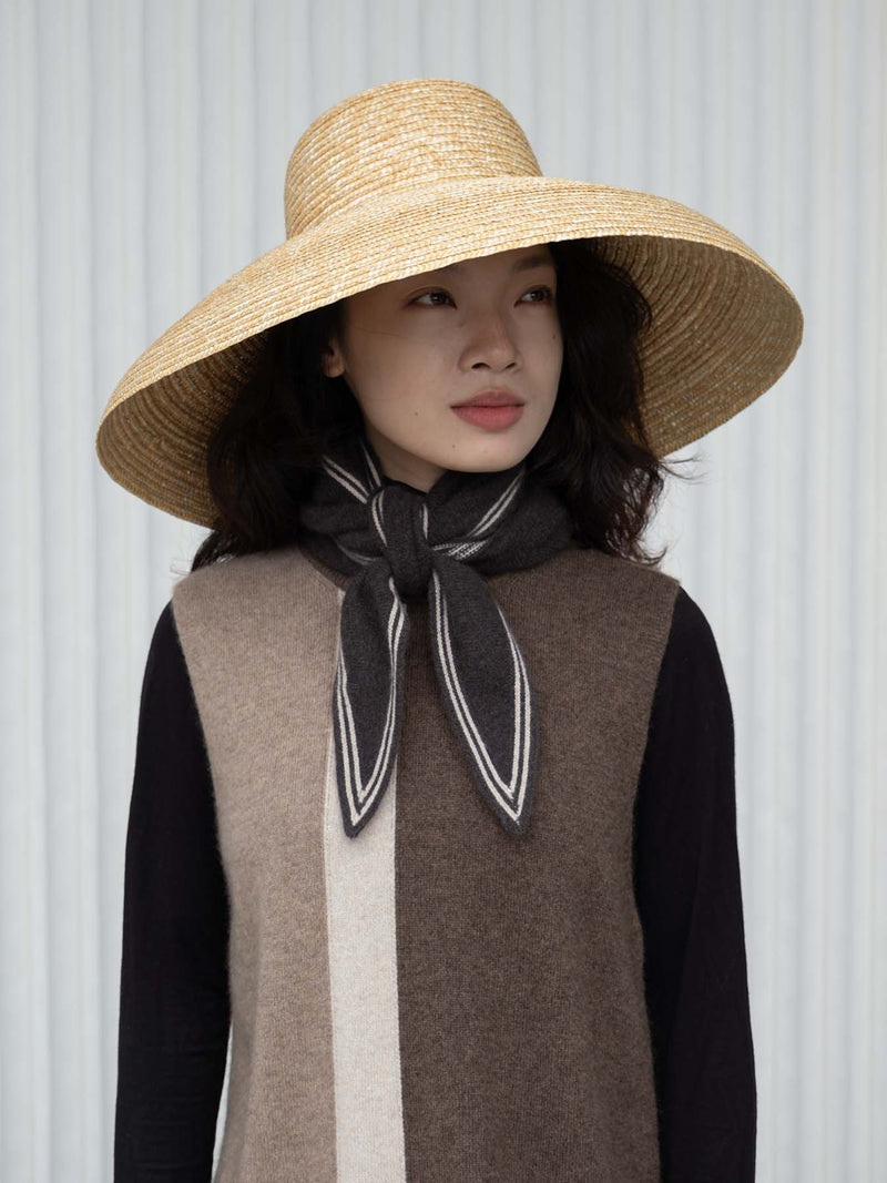 Person in a large straw hat wearing a dark brown scarf with white stripes over a brown and beige outfit.