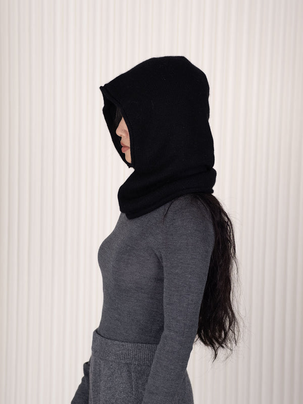Person wearing a black hood/balaclava aagainst a white background