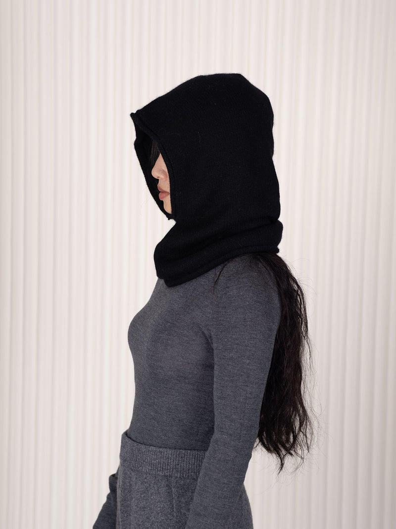 Person wearing a black hood/balaclava aagainst a white background