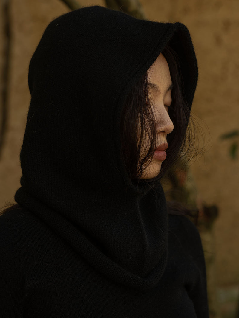 Person wearing a black hood against a blurred natural background
