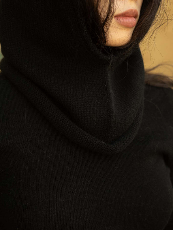 Person wearing a black hood/balaclava aagainst a tan background