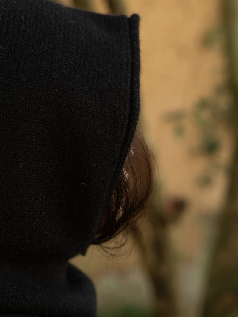 Person wearing a black hood/balaclava aagainst a tan background