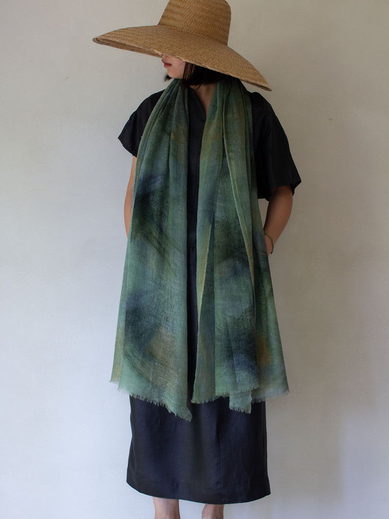 Person wearing a wide-brimmed hat and a green scarf against a plain background