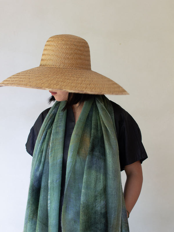 Person wearing a wide-brimmed straw hat and a green scarf against a white background