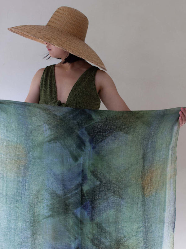 Woman holding a large green and blue patterned fabric against a plain background
