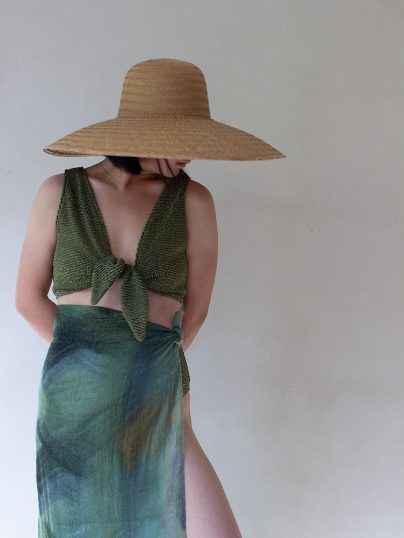 Person wearing a wide-brimmed straw hat and green top and skirt against a plain background