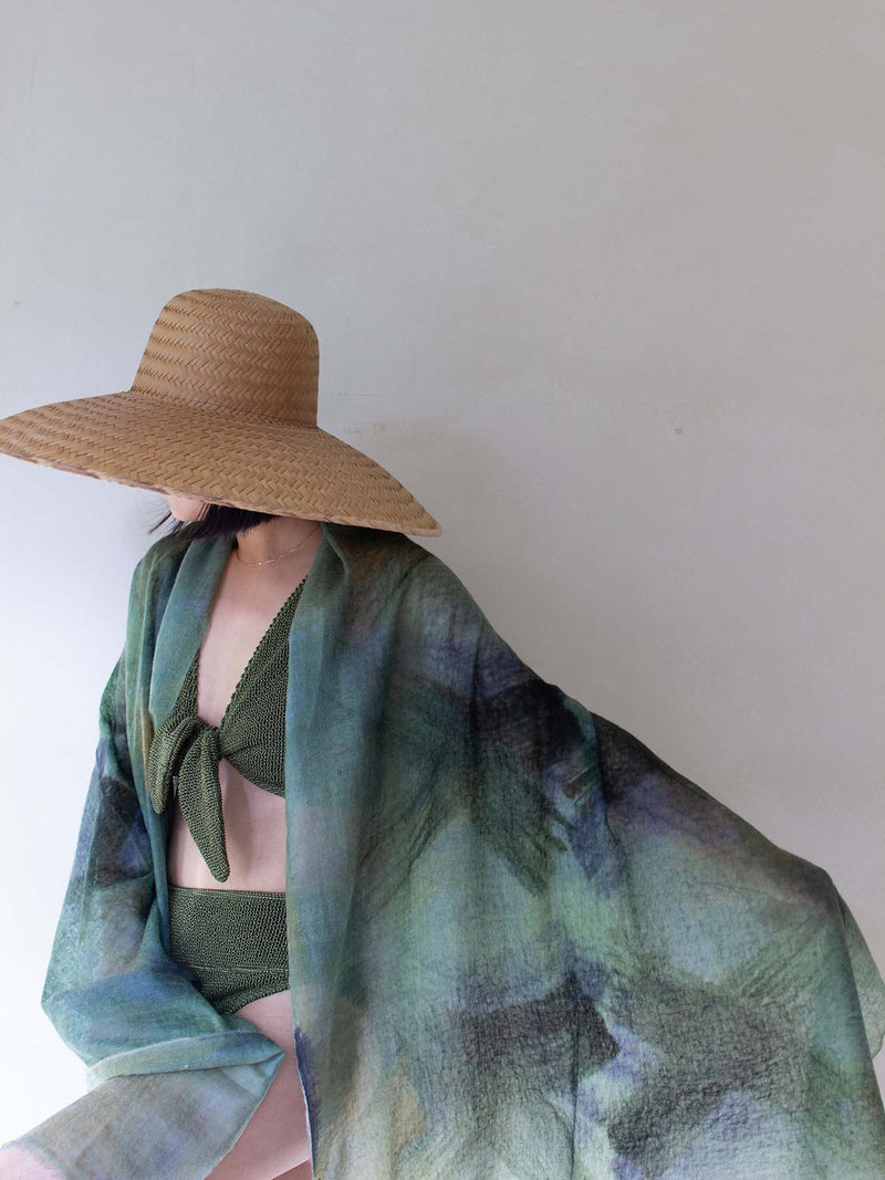 Person wearing a wide-brimmed hat and a green patterned shawl against a plain background