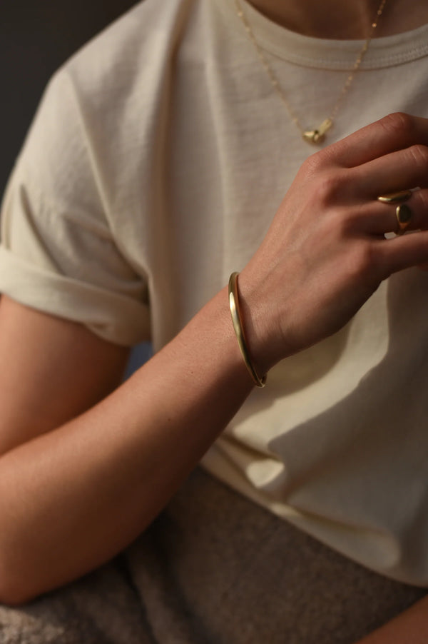 Close-up of a person wearing a brass bracelet and ring on a plain background