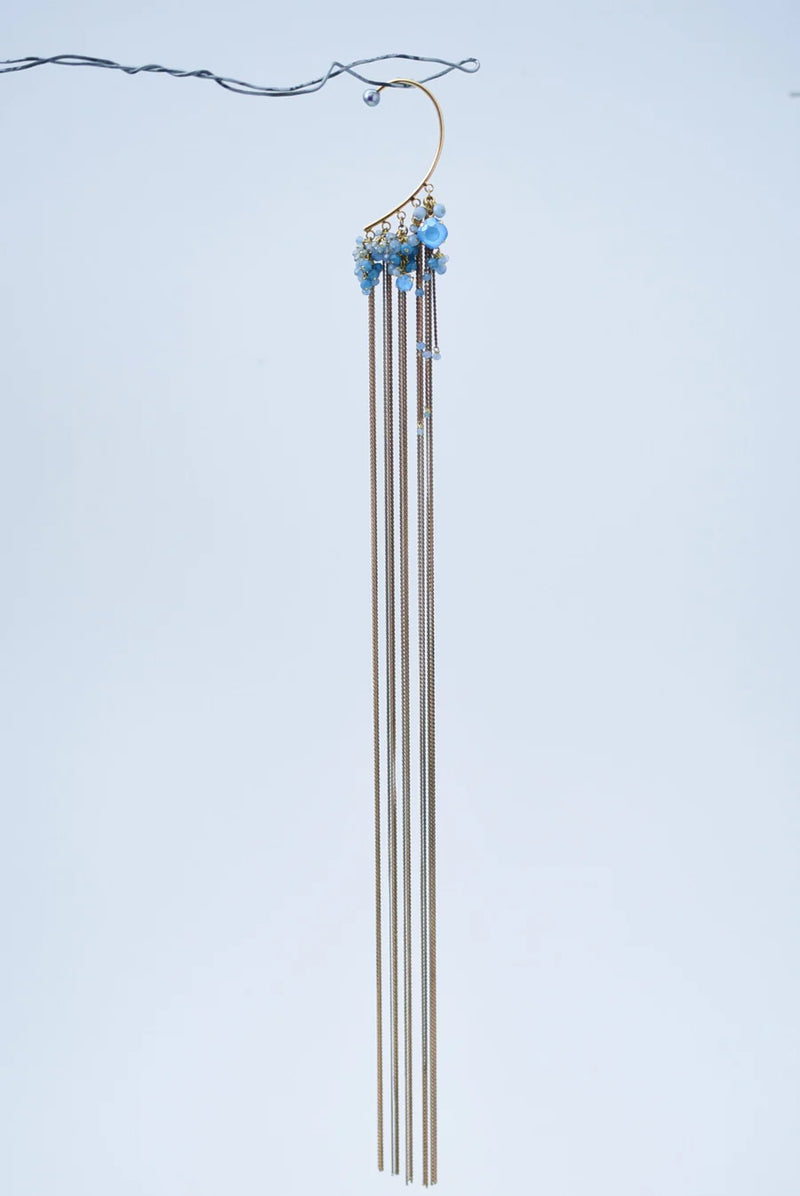 Ear cuff with brass chain fringe and blue stones on a white background handing on a wire