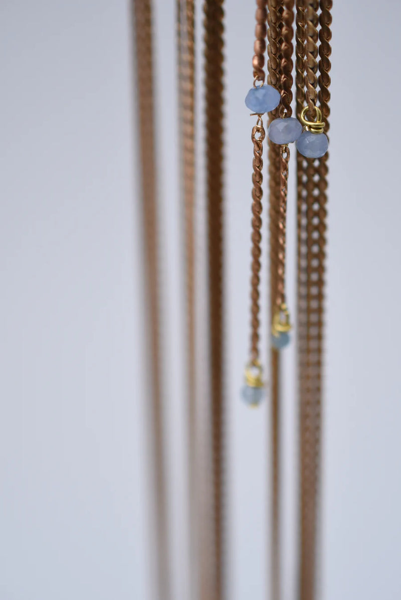 Close-up of a  ear cuff with brass chain fringe and blue stones on a white background