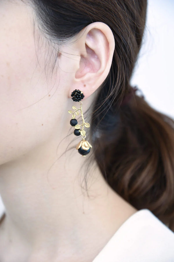 Close-up of a person wearing branching brass earrings with black beads.