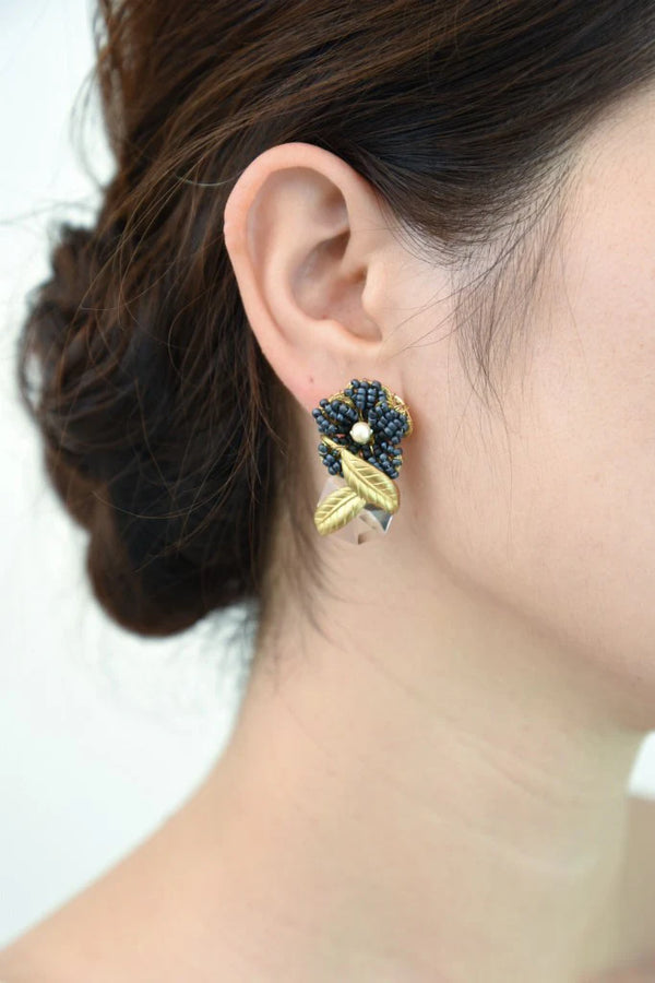 Close-up of a person wearing a floral earring with black beads and golden accents.