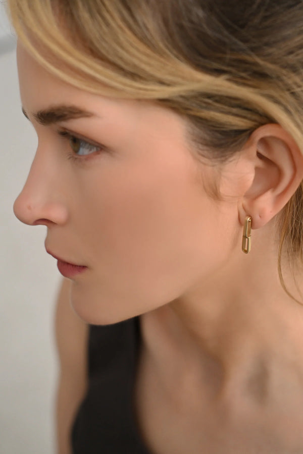 Close-up of a person wearing brass earrings with a neutral background