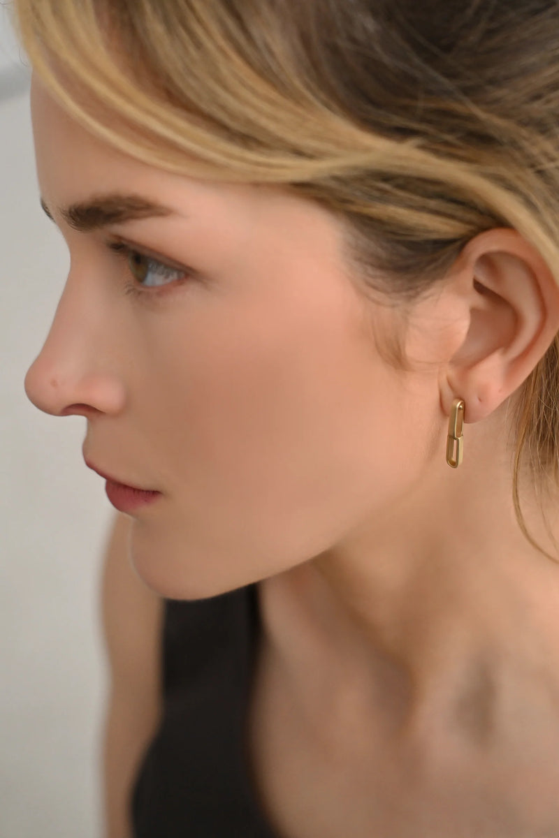 Close-up of a person wearing brass earrings with a neutral background