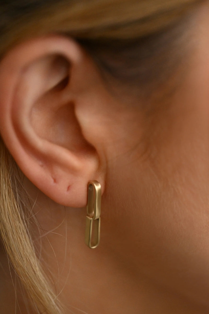 brass earring worn on a person's ear with a neutral background