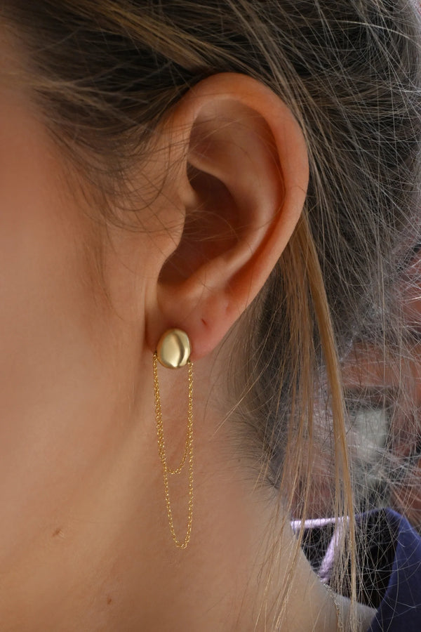 Close-up of a person wearing a brass earring with a dangling chain.