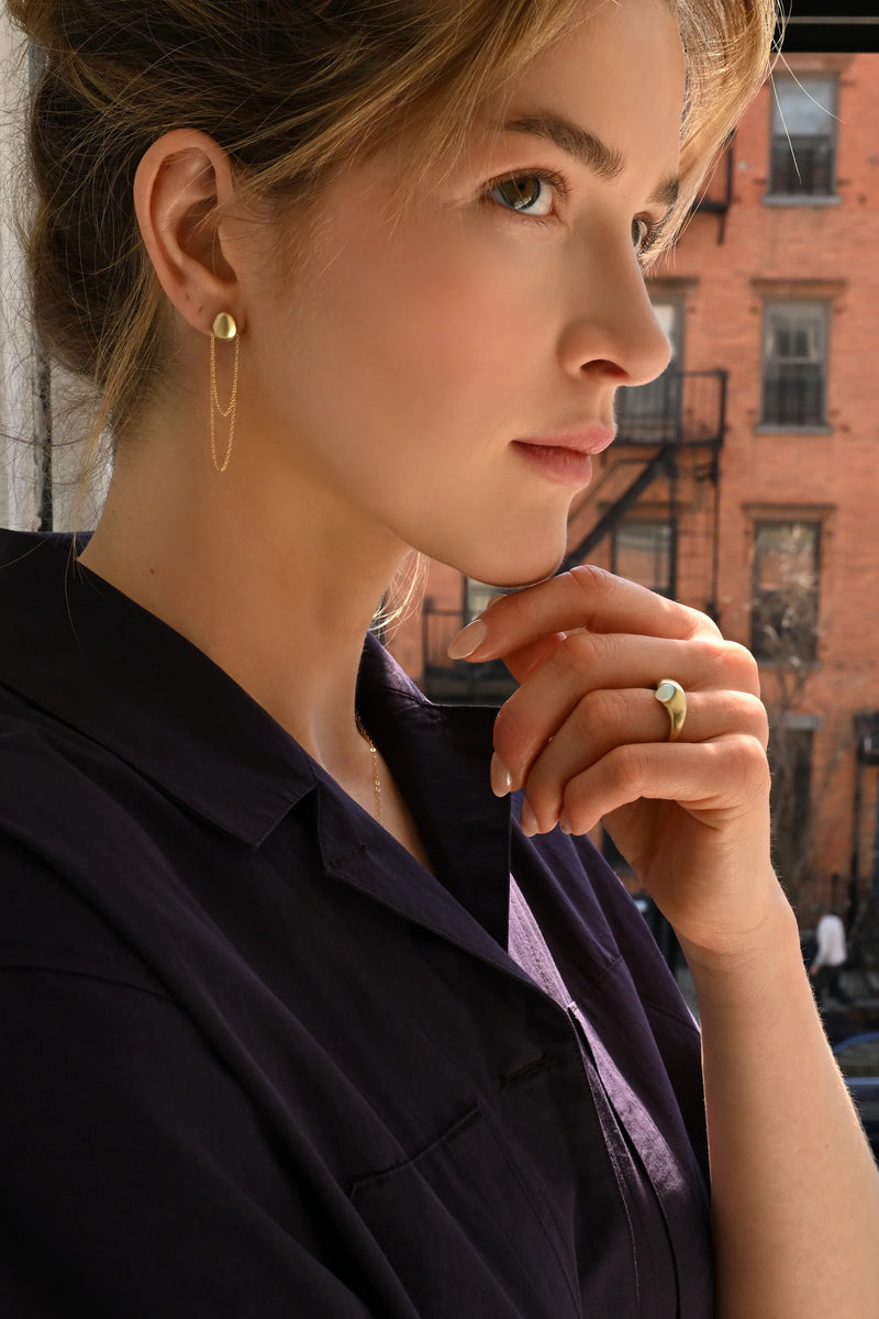 person wearing a brass earring with a dangling chain.