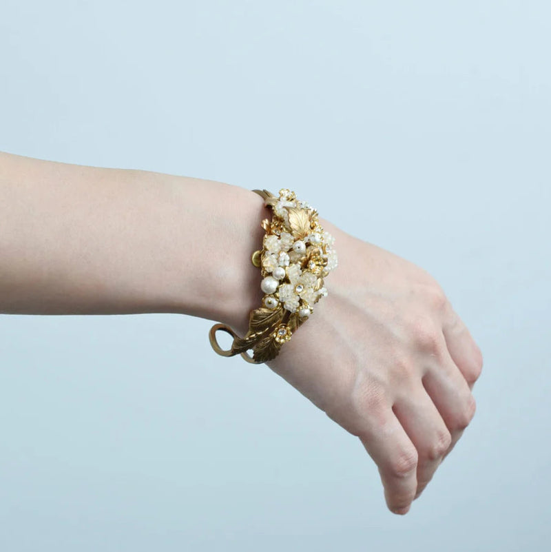 Hand wearing a gold bracelet with pearls on a light blue background