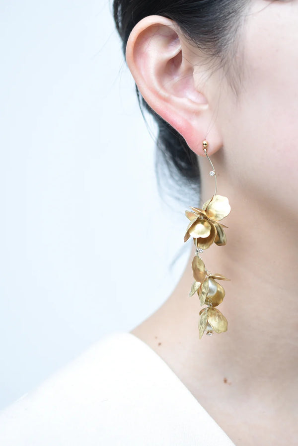 Person wearing a long chandelier earrings with hanging brass petals and pearl accents 