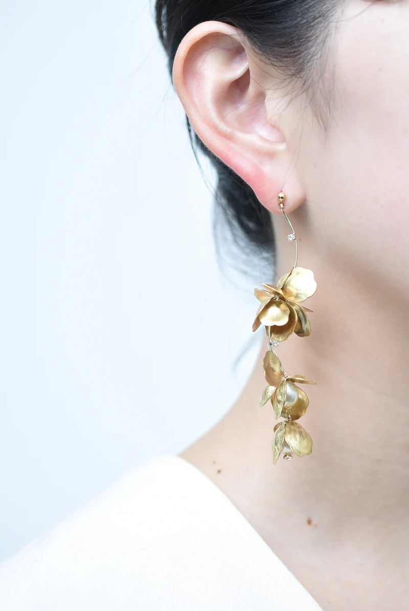 Person wearing a long chandelier earrings with hanging brass petals and pearl accents 