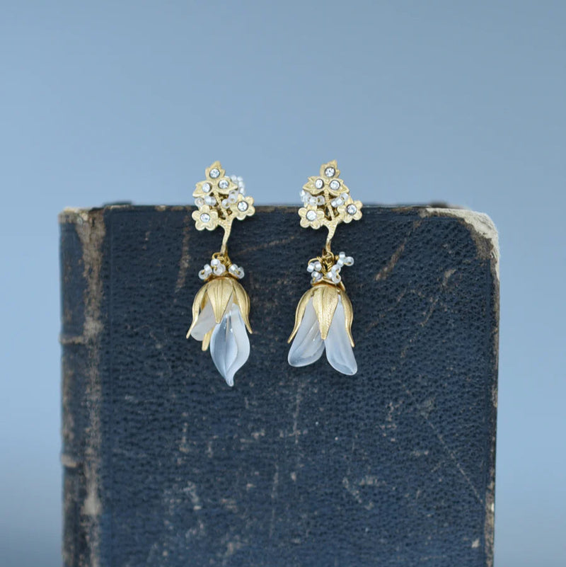 Brass, crystal, and lucite dangle earrings inspired by sweet pea blossoms on a textured background