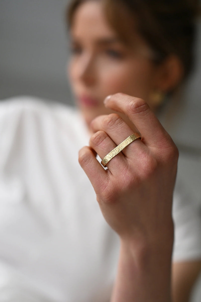 Close-up of a hand wearing a brass ring with a blurred background