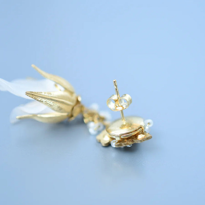 Back of a grass, crystal, and lucite dangle earring inspired by sweet pea blossoms on a textured background