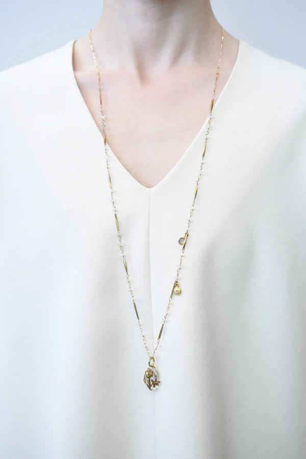 Person in white blouse wearing a a brass necklace with crystal accents and a glass and brass Poppy pendant 