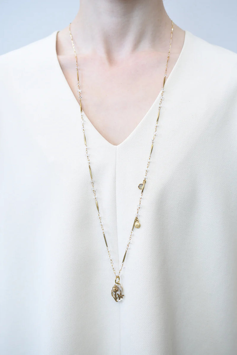 Person in white blouse wearing a a brass necklace with crystal accents and a glass and brass Poppy pendant 