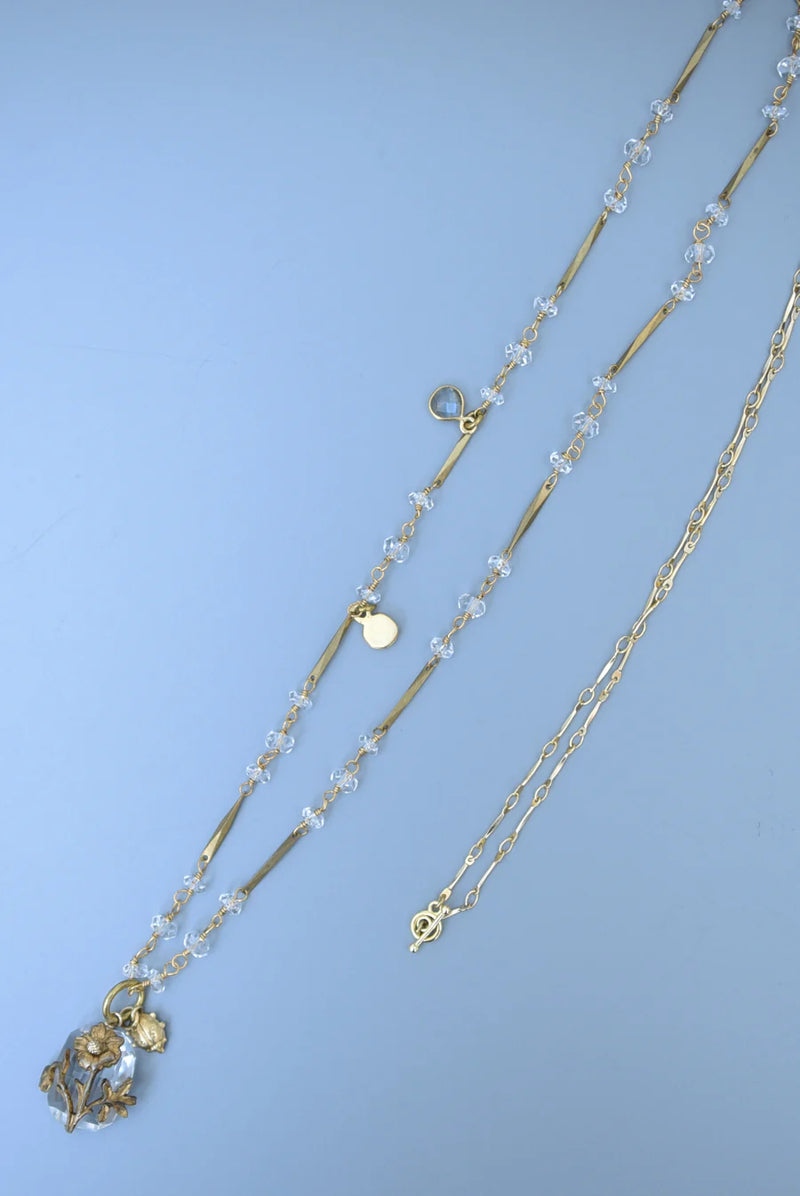 Brass necklace with crystal accents and a glass and brass Poppy pendant on a textured surface