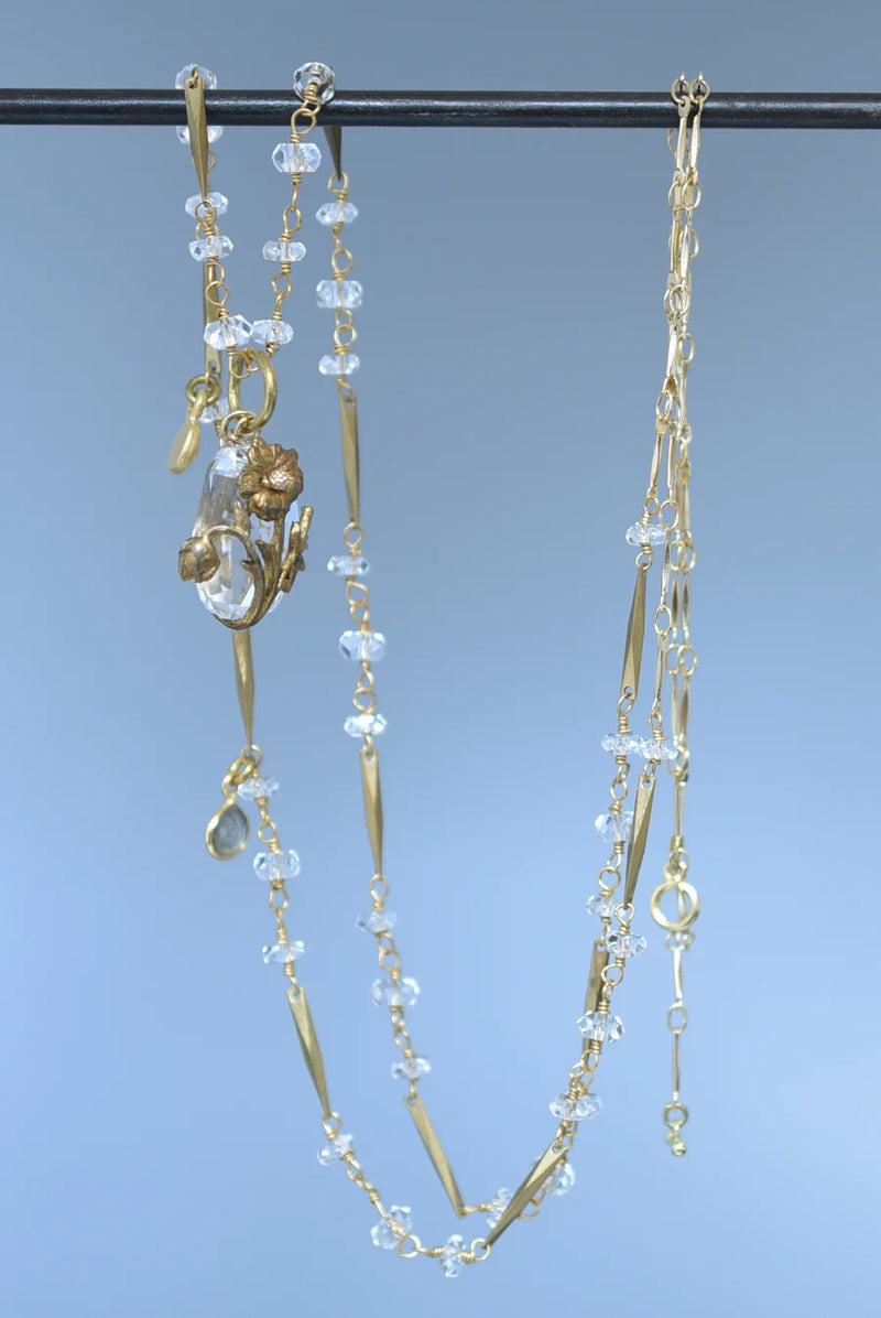 Brass necklace with crystal accents and a glass and brass Poppy pendant hanging against blue background