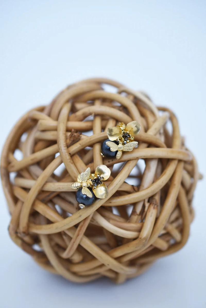 Brass bee and begonia blossom earrings on a woven wooden ball with a blurred background